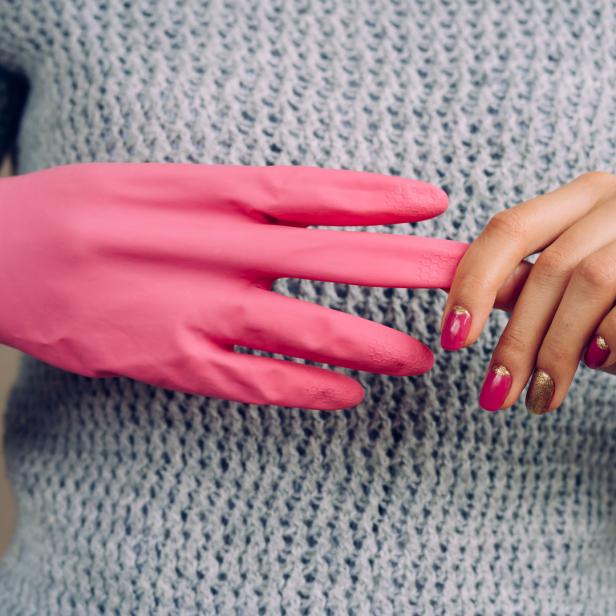 Eine Hand mit lackierten Nägeln zieht einen pinkfarbenen Gummihandschuh an.