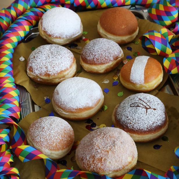 Neun Berliner Pfannkuchen, einige mit Puderzucker, liegen auf einem Tablett mit Karnevalsgirlande.