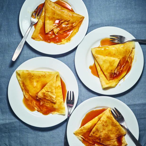 Vier Teller mit Crêpes und Karamellsauce auf einem grauen Tuch.