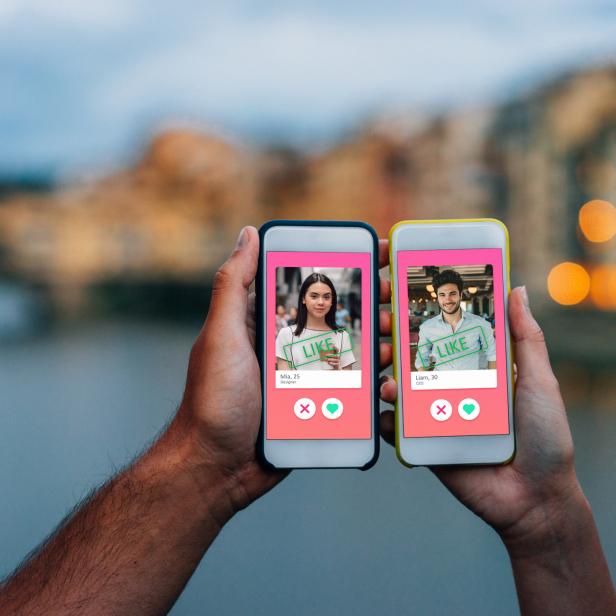 Eine Person hält zwei Smartphones mit Dating-App-Profilen vor einer Brücke.