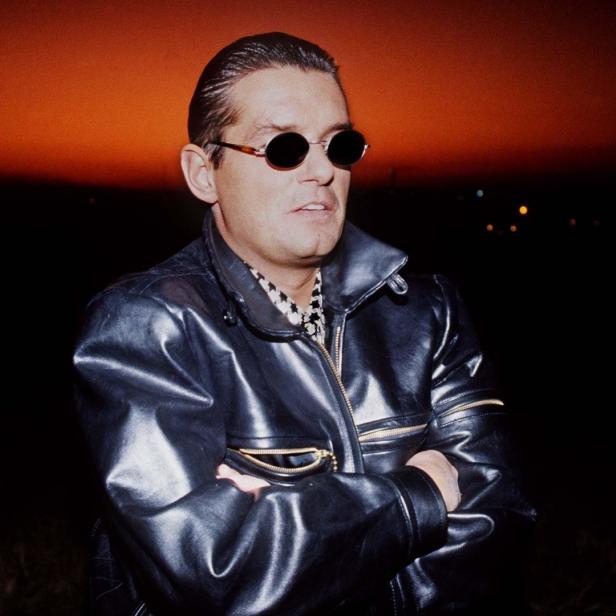 Ein Mann mit Sonnenbrille und Lederjacke vor einem orangefarbenen Himmel.