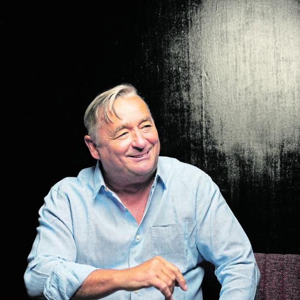 Ein lächelnder Mann mit hellblauem Hemd sitzt vor einem dunklen Hintergrund.
