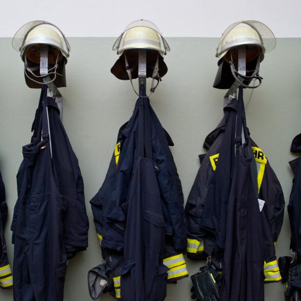 Mehrere Feuerwehrhelme und Uniformen hängen an Wandhaken in einer Reihe.