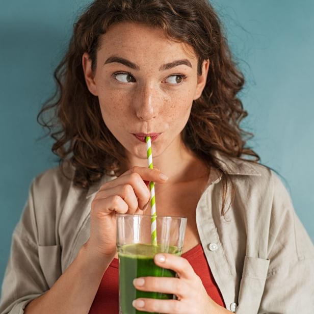 Eine Frau trinkt einen grünen Smoothie mit einem Strohhalm.