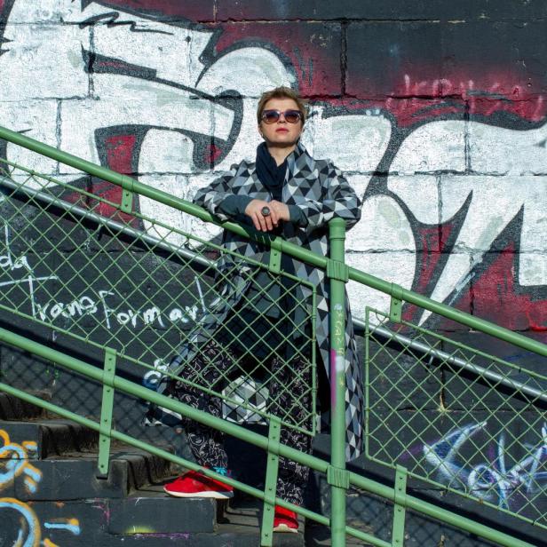 Eine Frau mit Sonnenbrille posiert auf einer Treppe vor einer Graffitiwand.