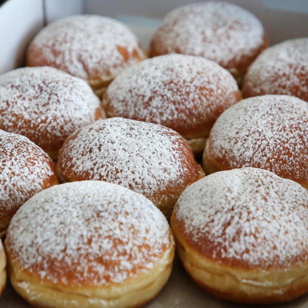 Mehrere Berliner Pfannkuchen mit Puderzucker in einer Schachtel.