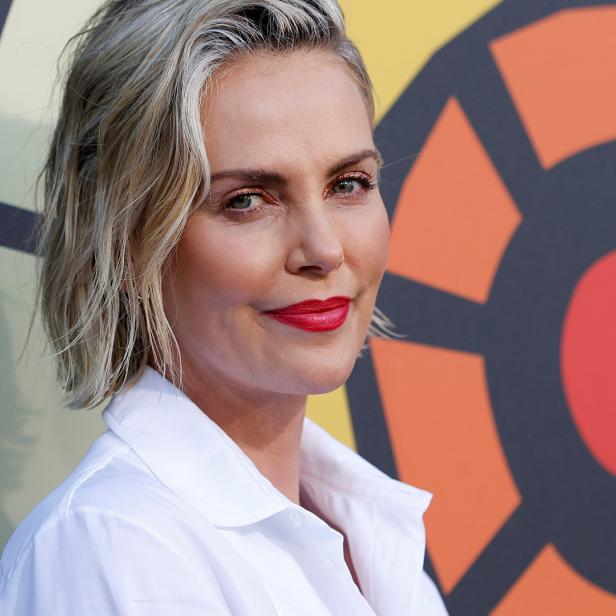 Ein Porträt von Charlize Theron mit rotem Lippenstift vor einem farbenfrohen Hintergrund.