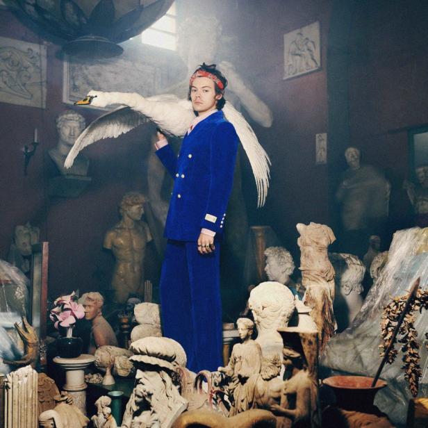 Harry Styles posiert mit einem Schwan in einem Raum voller Statuen.