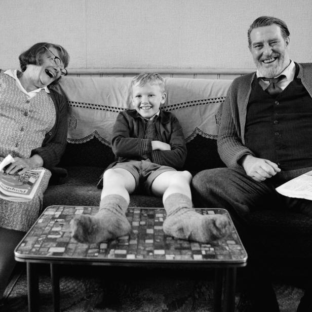 Schwarzweißaufnahme einer lachenden Familie, die auf einem Sofa sitzt.