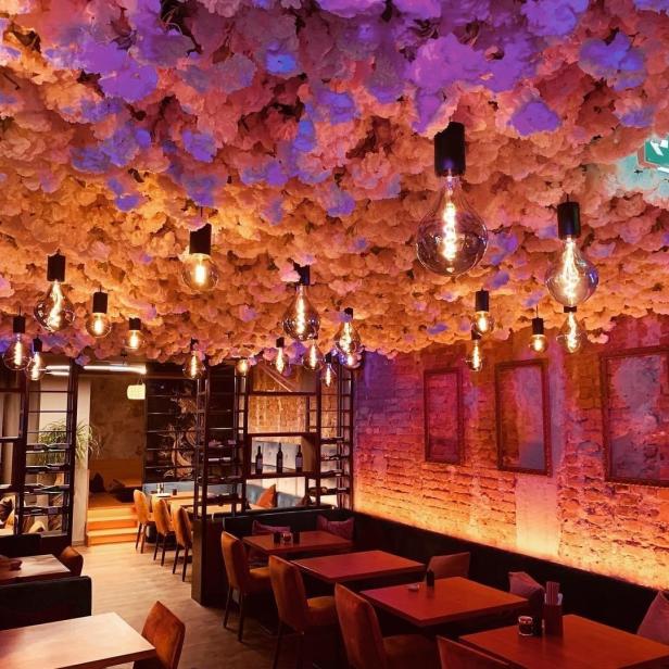 Ein Restaurant mit Blumendecke und Edison-Glühbirnen in warmem Licht.