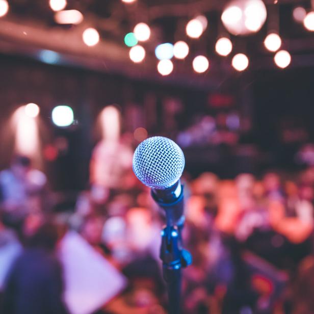 Event hall: Close up of microphone stand, seats with audience in the blurry background