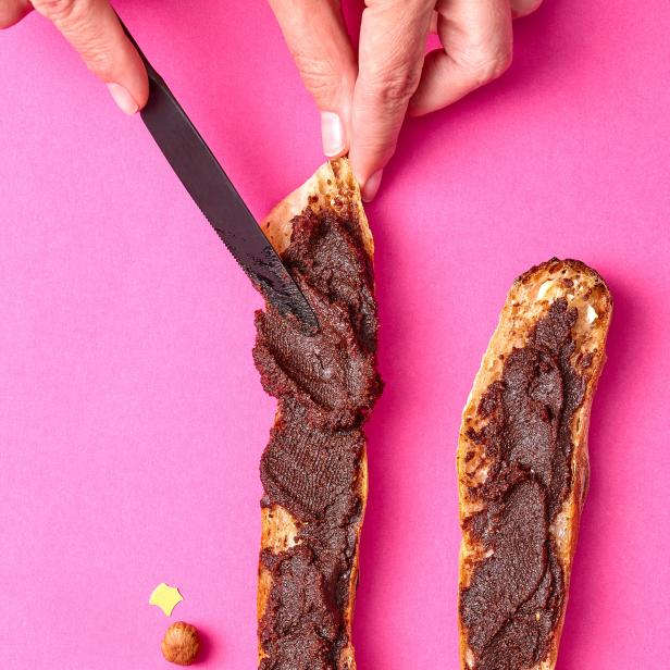 Zwei Brotscheiben mit Schokoladenaufstrich auf einem rosa Untergrund mit Konfetti.