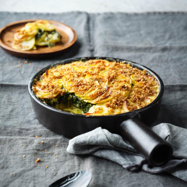 Ein Kartoffelgratin mit Spinat und einer Kruste in einer schwarzen Pfanne.