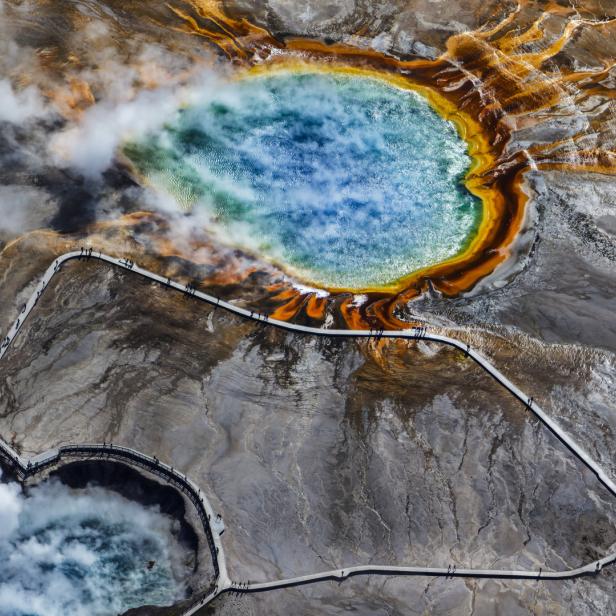 Luftaufnahme der farbenprächtigen Grand Prismatic Spring im Yellowstone-Nationalpark mit Besuchern auf einem Holzsteg.
