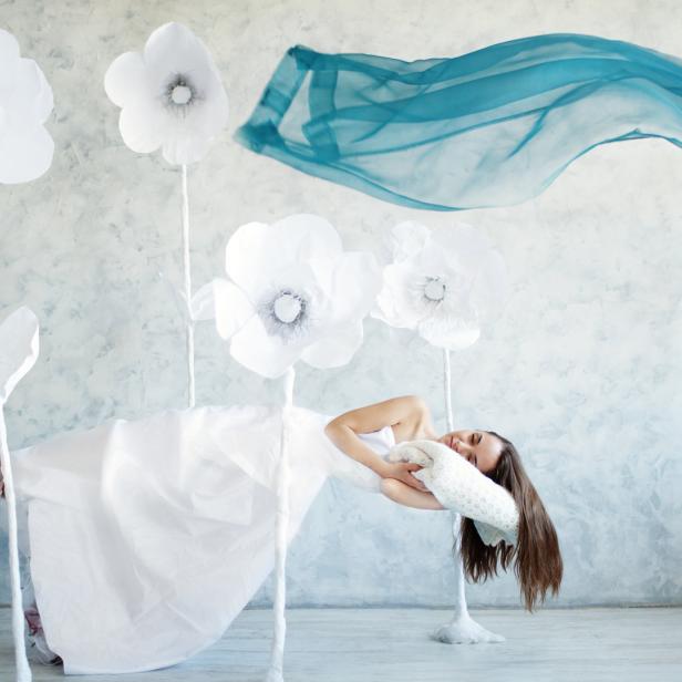Eine Frau in einem weißen Kleid liegt auf einer Schaukel, umgeben von Papierblumen und einem blauen Tuch.
