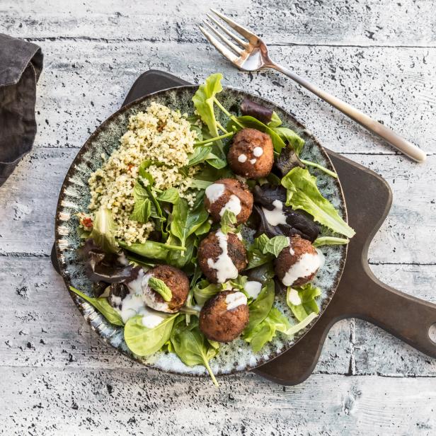 Ein Teller mit Salat, Falafel und Couscous auf einem Holztisch.