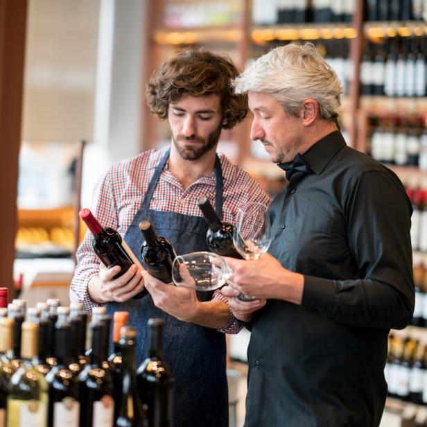 Zwei Männer betrachten Weinflaschen in einem Weinladen.