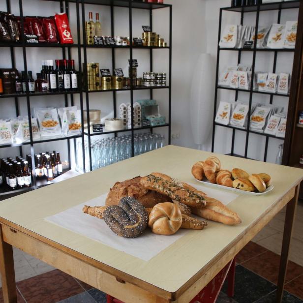 In einem Laden steht ein Tisch mit Brot und Brötchen vor Regalen mit Lebensmitteln.