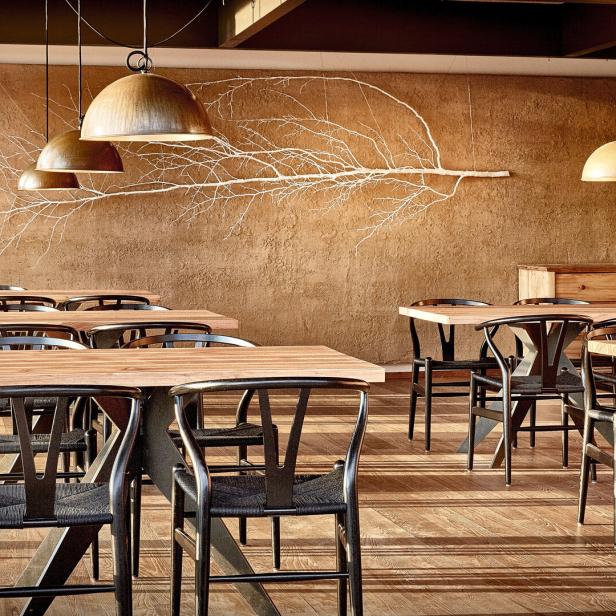 Ein Restaurant mit Holztischen, schwarzen Stühlen und einer Wanddekoration in Form eines Astes.