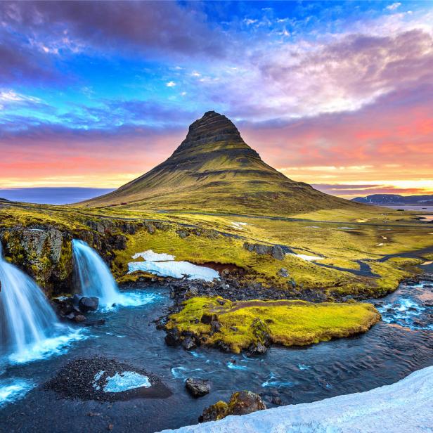 Der Berg Kirkjufell und ein Wasserfall in Island unter einem farbenprächtigen Himmel.