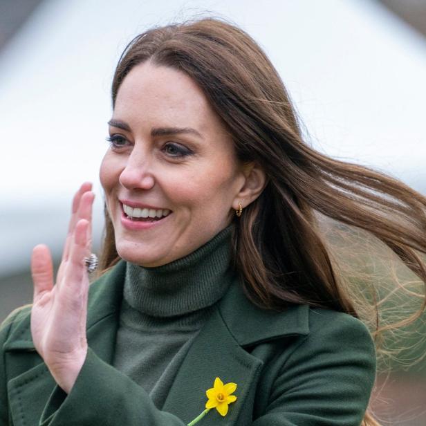Kate Middleton lächelt und winkt mit einer Narzisse an ihrem Mantel.