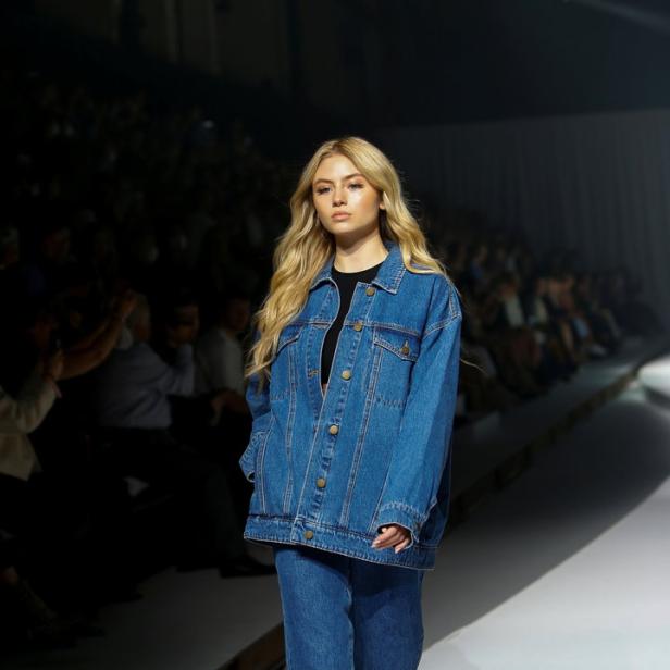 Eine blonde Frau in Jeansjacke und Jeans läuft auf einem Laufsteg.