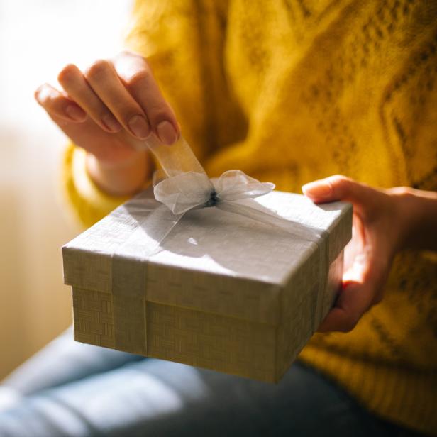 Eine Person in einem gelben Pullover öffnet ein Geschenk mit einer silbernen Schleife.