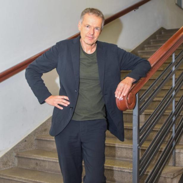 Ein Mann in einem schwarzen Anzug steht auf einer Treppe und lehnt sich an das Geländer.