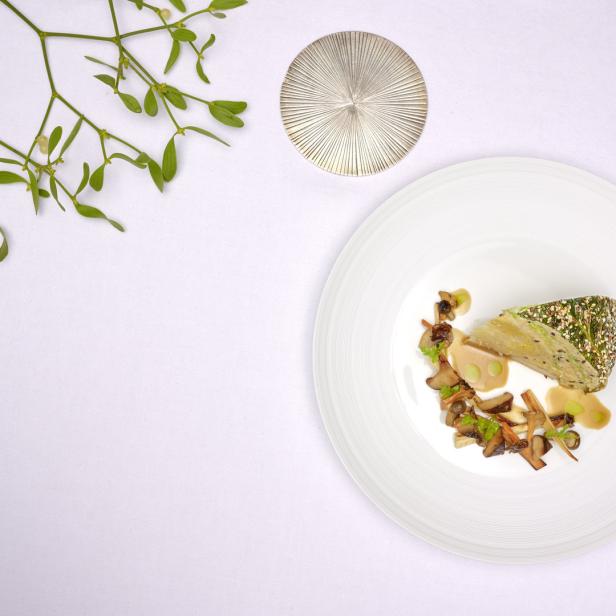 Ein Teller mit einer Gemüseterrine, Pilzen und einer hellen Sauce, garniert mit Mistelzweigen.
