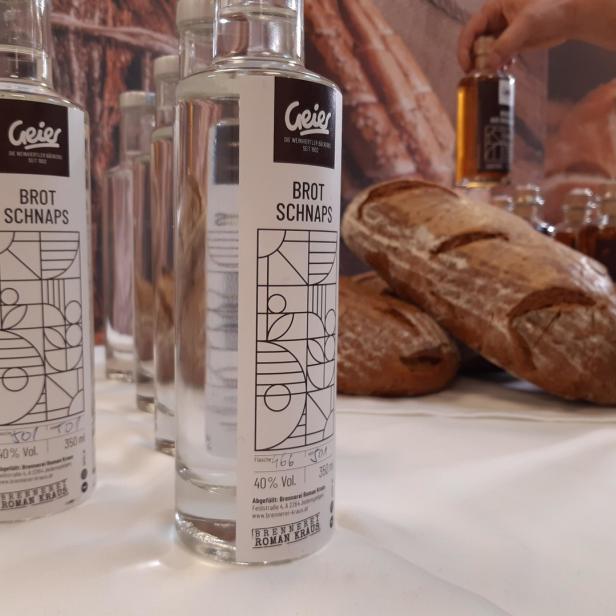 Mehrere Flaschen „Geier Brot Schnaps“ stehen auf einem Tisch neben Brotlaiben.