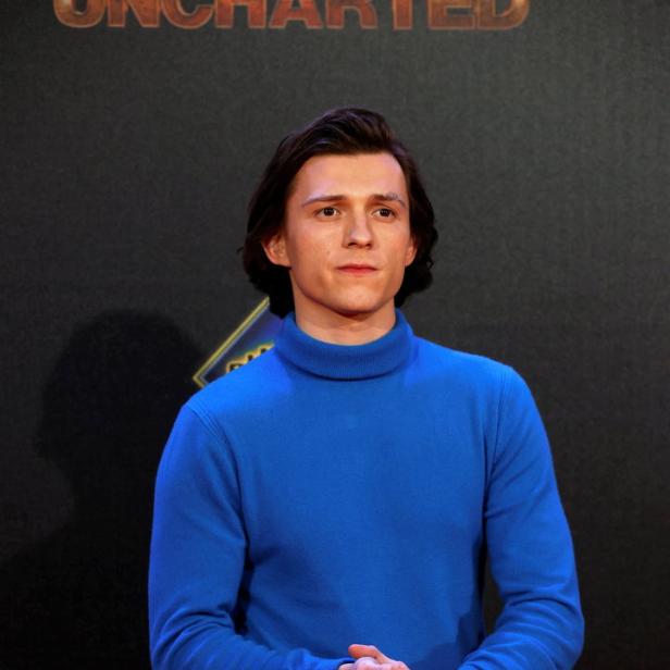 Tom Holland posiert vor einer Wand mit dem Schriftzug „Uncharted“.