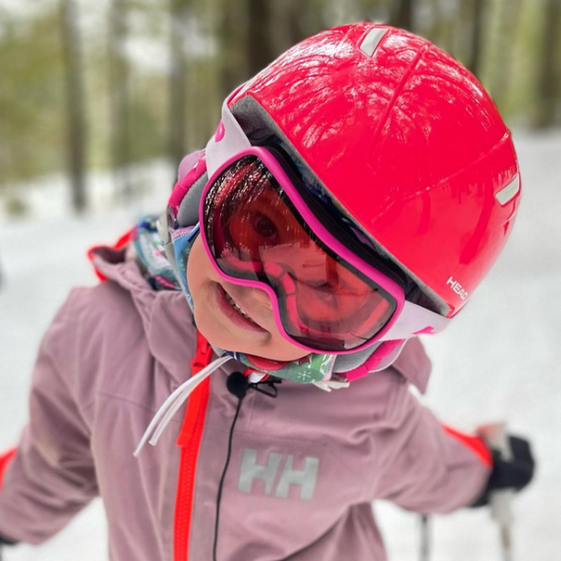Ein Kind mit rotem Skihelm und Skibrille steht im Schnee.