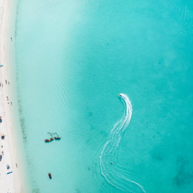 Luftaufnahme eines tropischen Strandes mit türkisfarbenem Wasser und einem Jetski.