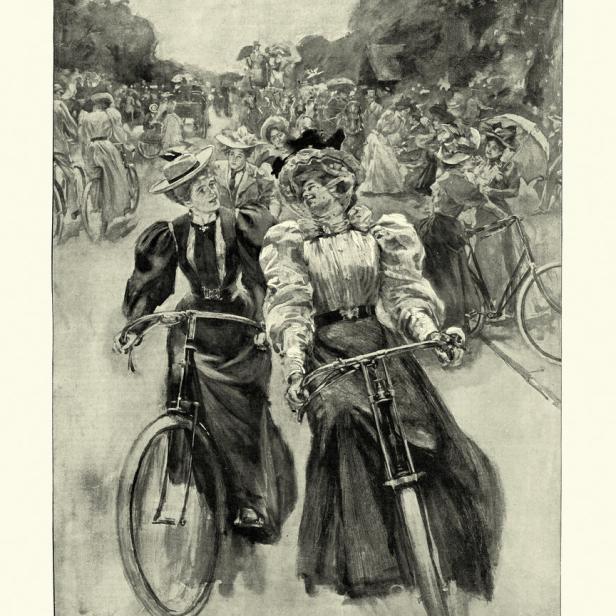 Zwei elegant gekleidete Frauen fahren im Battersea Park Fahrrad.