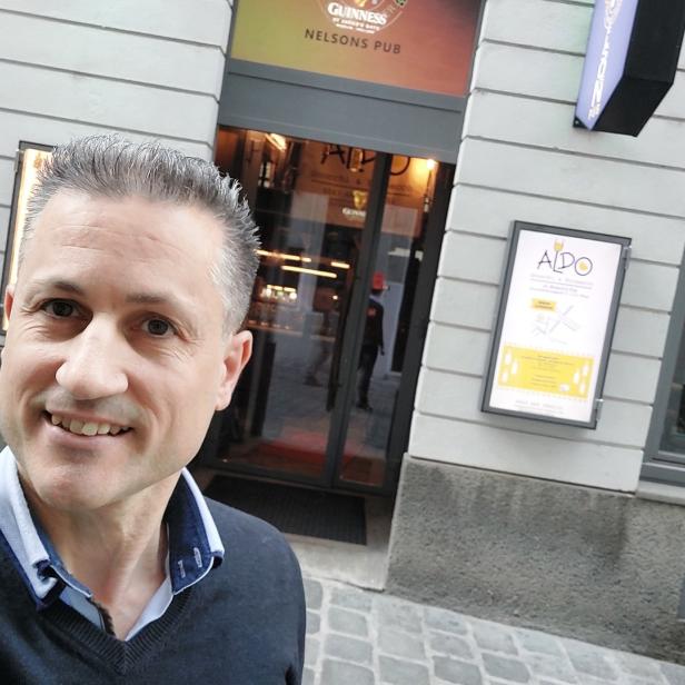 Ein lächelnder Mann vor „Nelson's Pub“ in einer Stadt.