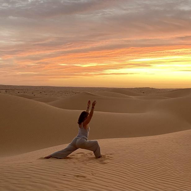 Eine Frau macht Yoga in der Wüste bei Sonnenuntergang.
