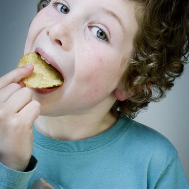 Ein Kind isst eine Kartoffelchips aus einer geöffneten Tüte.