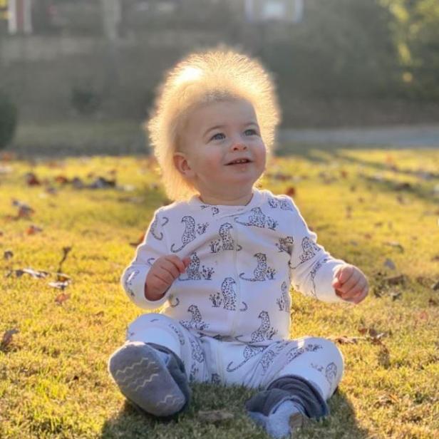 Ein Baby sitzt im Gras und schaut lächelnd nach oben.