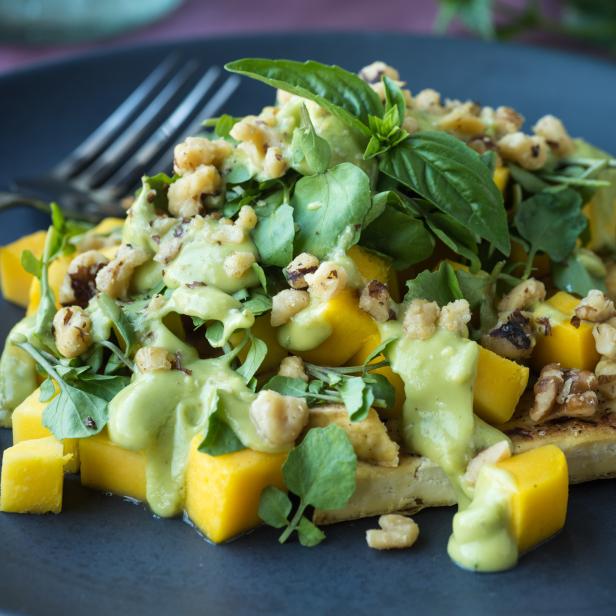 Ein Teller mit Mango, Tofu, Brunnenkresse, Walnüssen und einer grünen Soße.