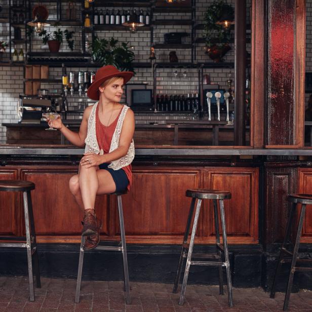 Eine Frau sitzt an einer Bar und hält ein Glas in der Hand.