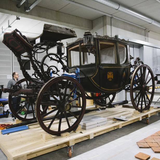 Eine historische Kutsche steht auf einer hölzernen Plattform in einem Lagerraum.