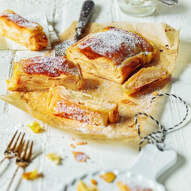 Apfelstrudelstücke, mit Puderzucker bestäubt, liegen auf einem Tisch.