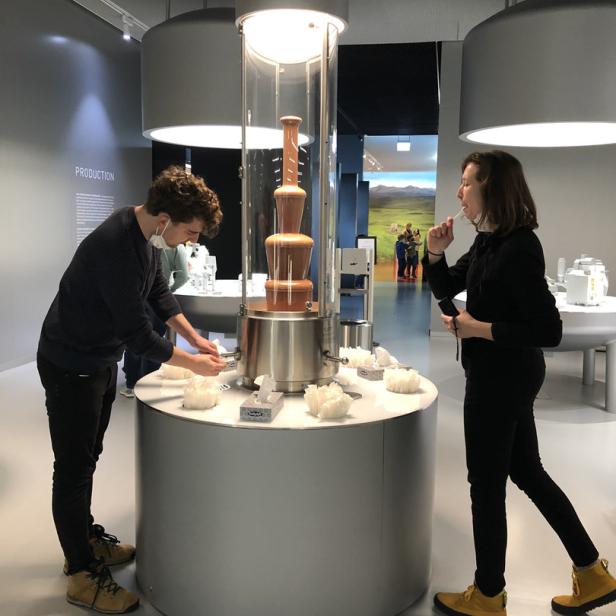Zwei Personen stehen an einem Schokoladenbrunnen in einem Museum.