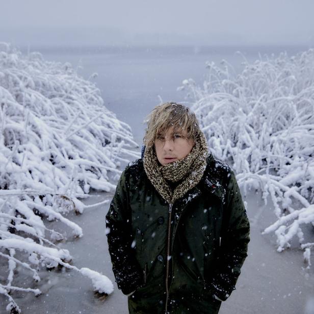 Ein Mann mit Schal und Jacke steht im Schnee zwischen schneebedeckten Pflanzen.