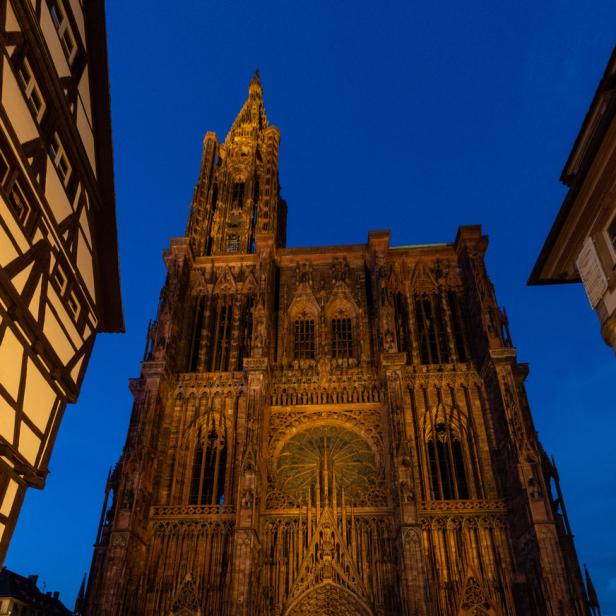 Die Fassade des Straßburger Münsters bei Dämmerung, mit Menschen davor.