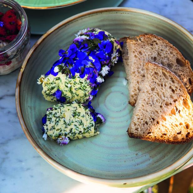 Ein Teller mit Kräuterbutter, dekoriert mit Blüten, und Brot.