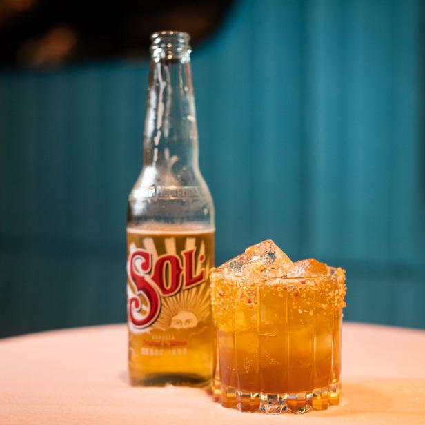 Eine Flasche Sol-Bier neben einem Cocktail mit Eiswürfeln und einem dekorierten Glasrand.