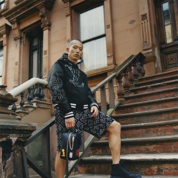 Ein Mann in einer Louis Vuitton Jacke und Shorts steht auf einer Treppe vor einem Gebäude.