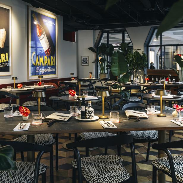 Ein elegantes Restaurant mit gedeckten Tischen und Campari-Werbeplakaten.