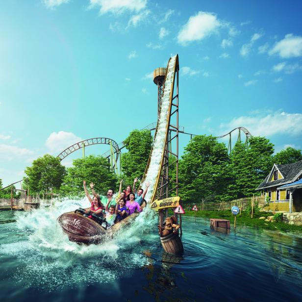 Eine Gruppe von Menschen fährt mit einem Baumstammboot eine Wasserachterbahn hinunter.